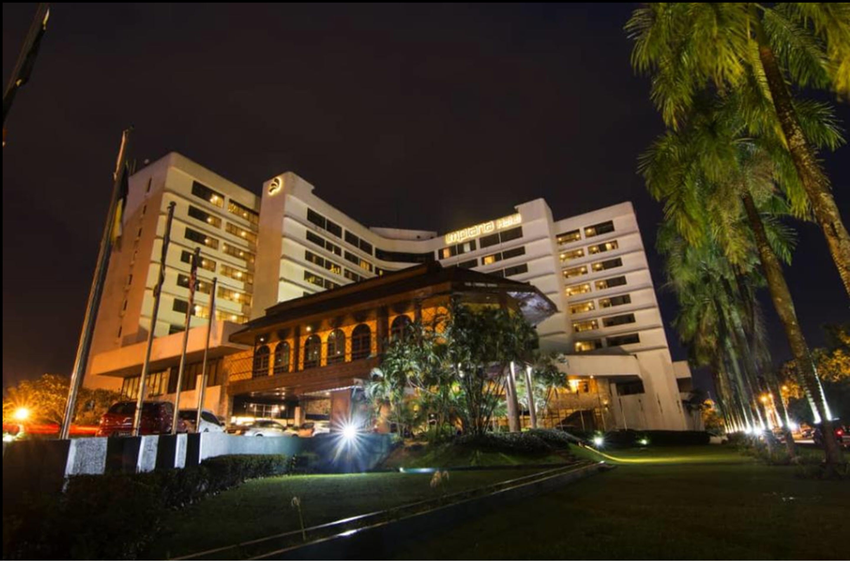 A multi-story hotel with a central courtyard, surrounded by palm trees and well-lit at night.