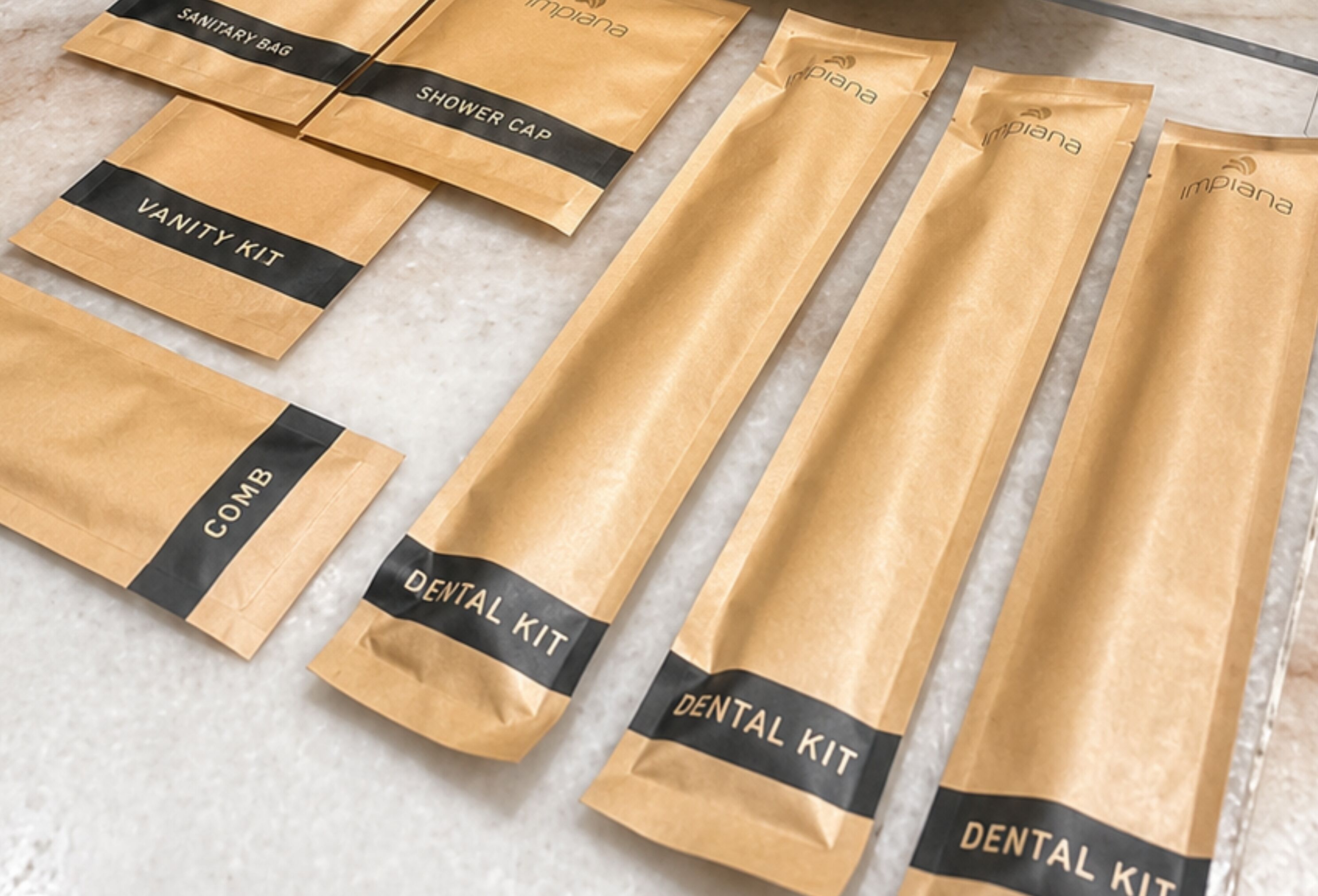 Several brown paper bags with black labels, each labeled with different items such as 'SANITARY BAG,' 'SHOWER CAP,' 'VANITY KIT,' 'COMB,' and 'DENTAL KIT.'
