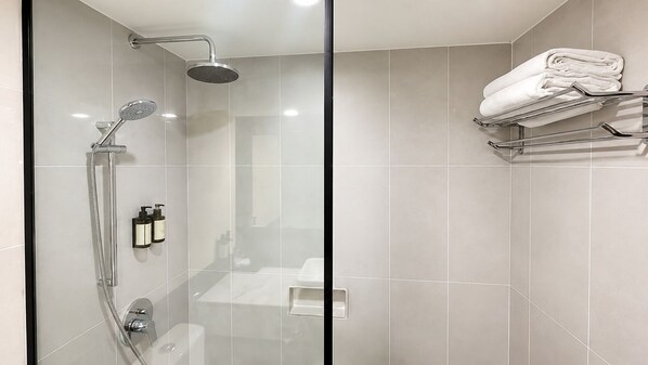 A modern bathroom with a glass shower enclosure, a towel rack with folded towels, and a visible toilet.