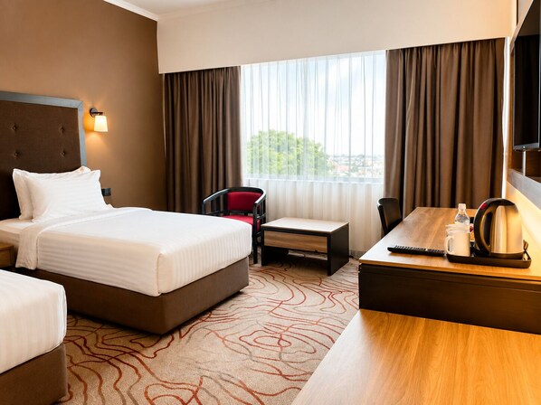 A hotel room with a large bed, a desk with a kettle, a chair, and a TV.