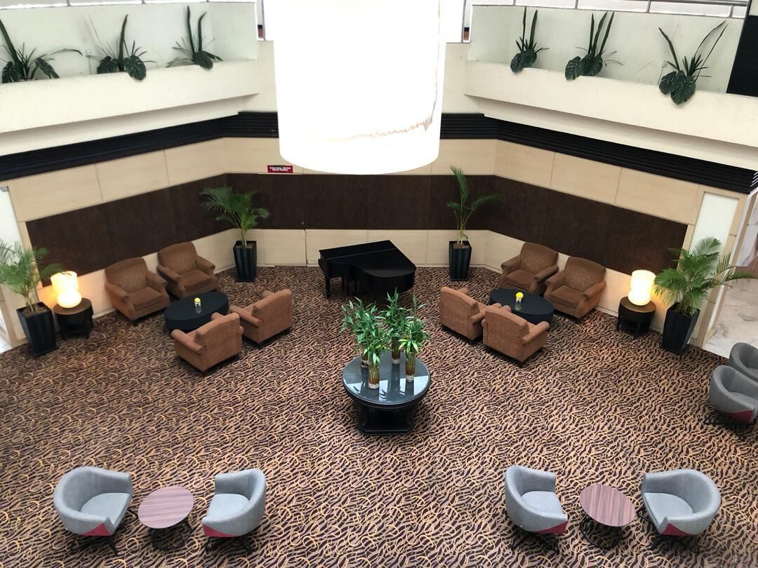 Een ontvangsthal met een kamerbreed tapijt, meerdere zithoeken met banken en stoelen, en potplanten.