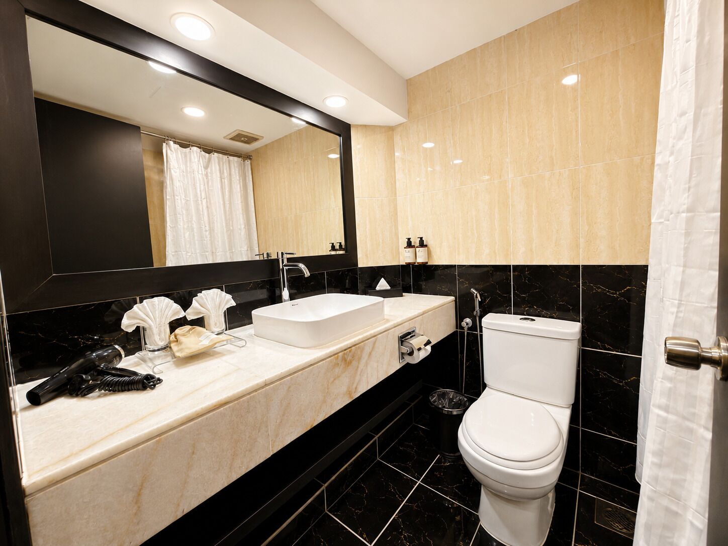 Un baño moderno con un espejo grande, un lavabo blanco, un inodoro y una zona de ducha.