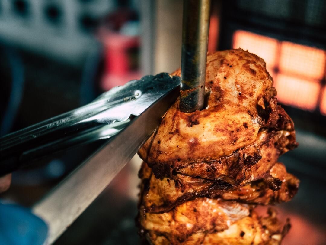 A close-up of a rotisserie chicken being carved with tongs.