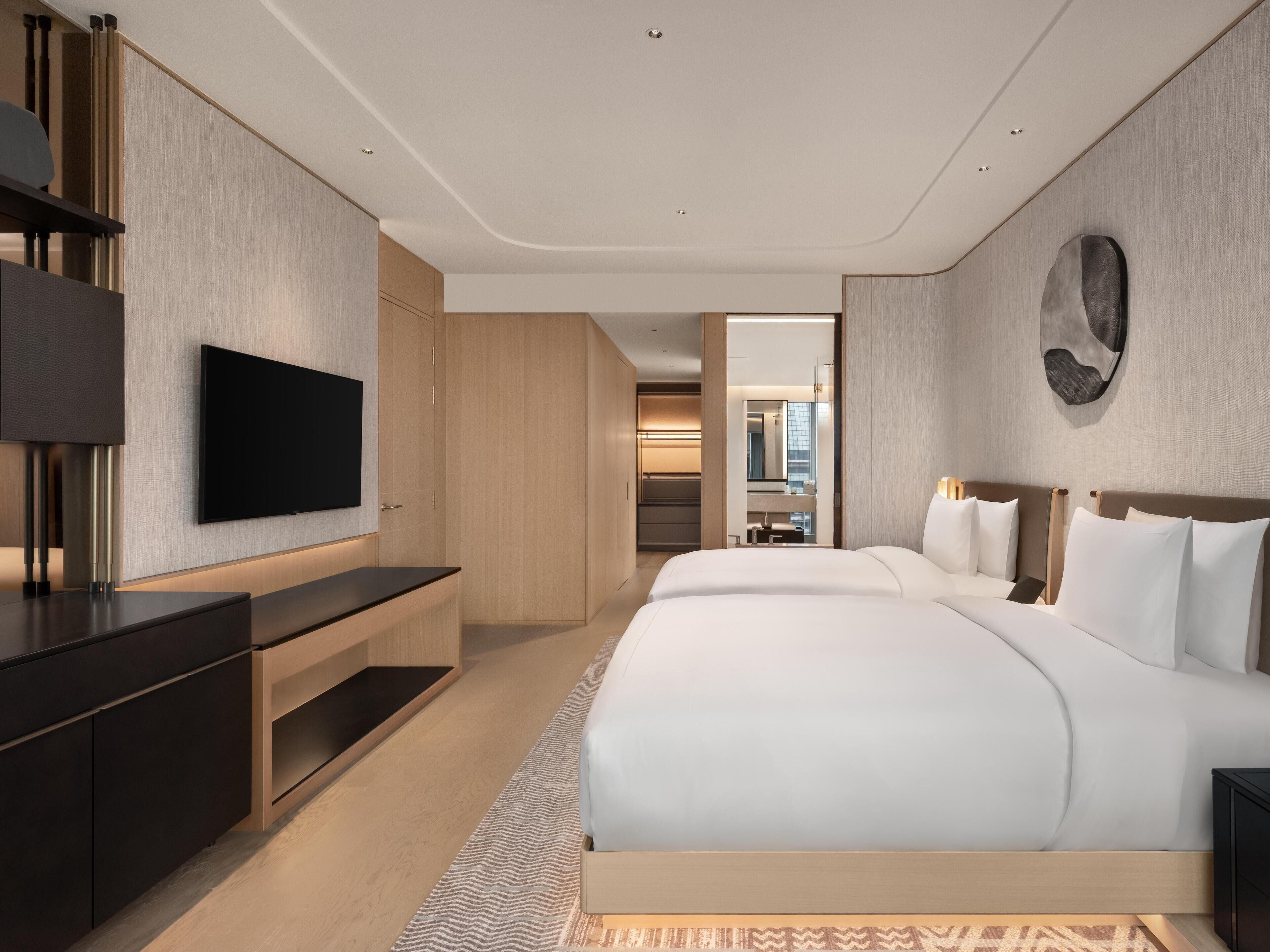 A modern hotel room with a large bed, a flat-screen TV, a desk, and a walk-in closet.