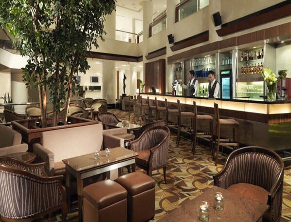 A spacious bar area with multiple seating options, including bar stools and cushioned chairs, and a large tree providing a natural element. - Conrad Kuala Lumpur (Kuala Lumpur)