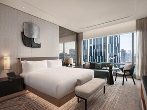A modern hotel room with a large bed, a sofa, a small table, and a view of the city through large windows. - Conrad Kuala Lumpur (Kuala Lumpur)