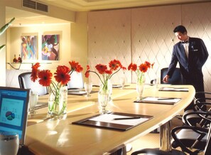 A conference room with a long table, vases with red flowers, and a man in a suit standing by the table. - Conrad Kuala Lumpur (Kuala Lumpur)