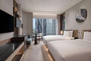 Habitación de hotel moderna con una cama grande, un escritorio, una silla, un televisor y vistas a edificios altos.