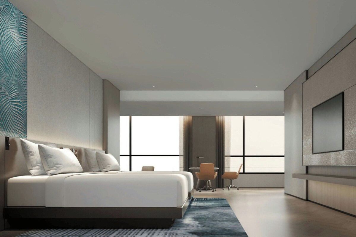 A modern hotel room with a large bed, a desk, and a view through the window.