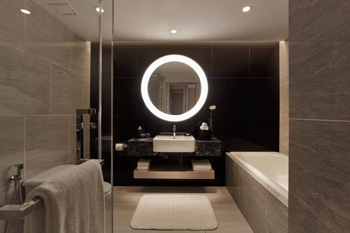 A modern bathroom with a round mirror, a sink, a bathtub, and a shower.