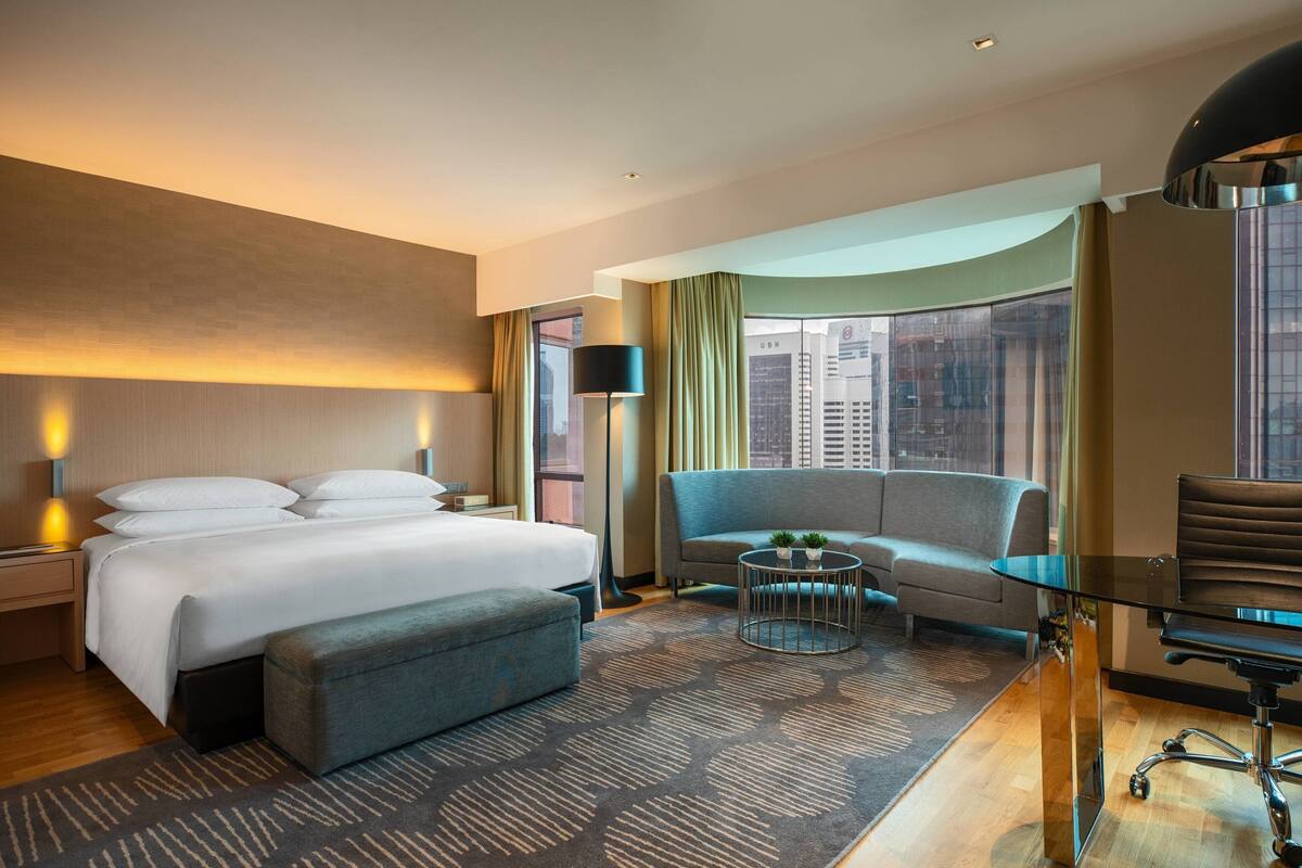 A hotel room with a large bed, a sofa, a desk, and a view of the city.