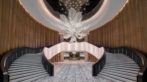 Een statige lobby met een centrale trap, een grote kroonluchter en een modern receptiebalie.