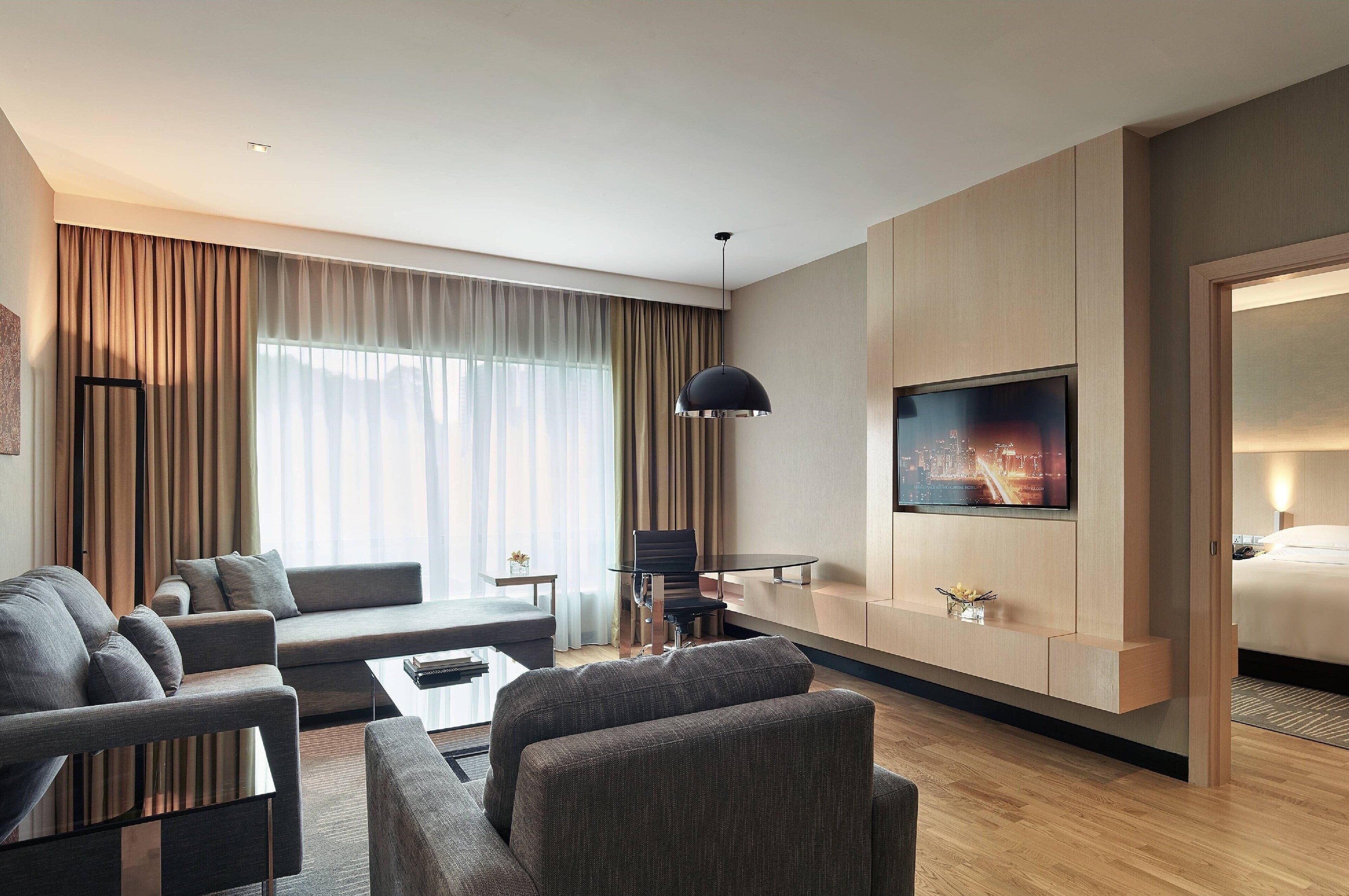 Una habitación de hotel moderna con sofá, sillones, una mesita, televisión y cama.
