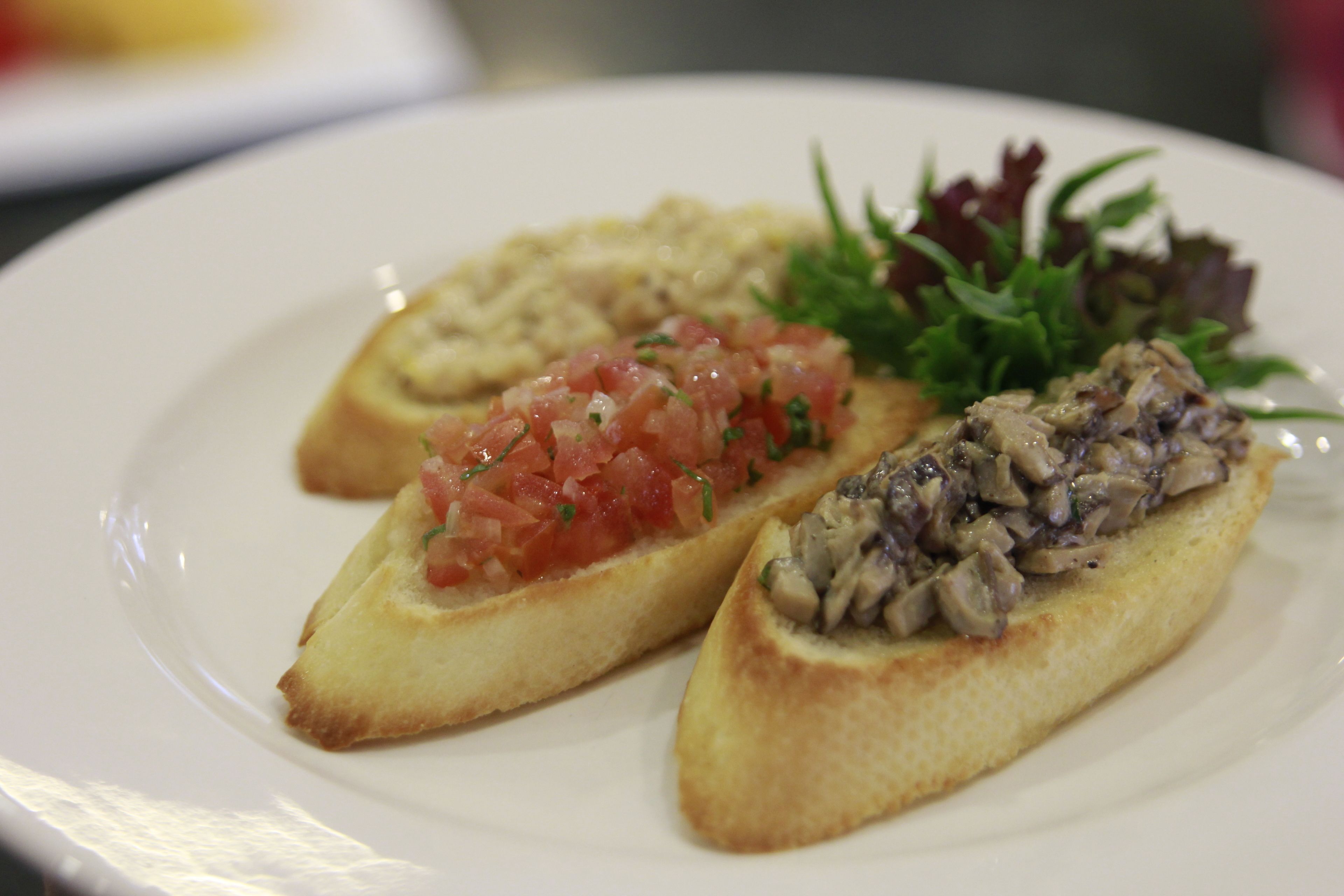 A plate with two open-faced sandwiches, one with a tomato topping and the other with a mushroom topping, accompanied by a small salad.