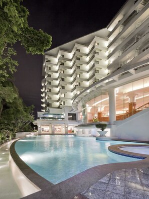 A modern hotel with a large indoor swimming pool, multiple balconies, and a well-lit lobby area.