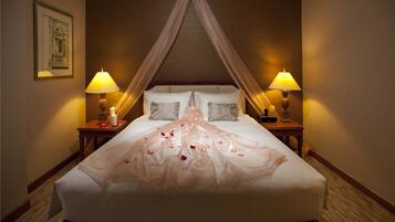A hotel room with a large bed, two bedside lamps, a canopy bed, and a framed picture on the wall.
