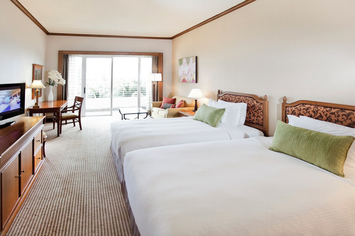 Een hotelkamer met twee bedden, een bureau, een televisie en een balkon met uitzicht.