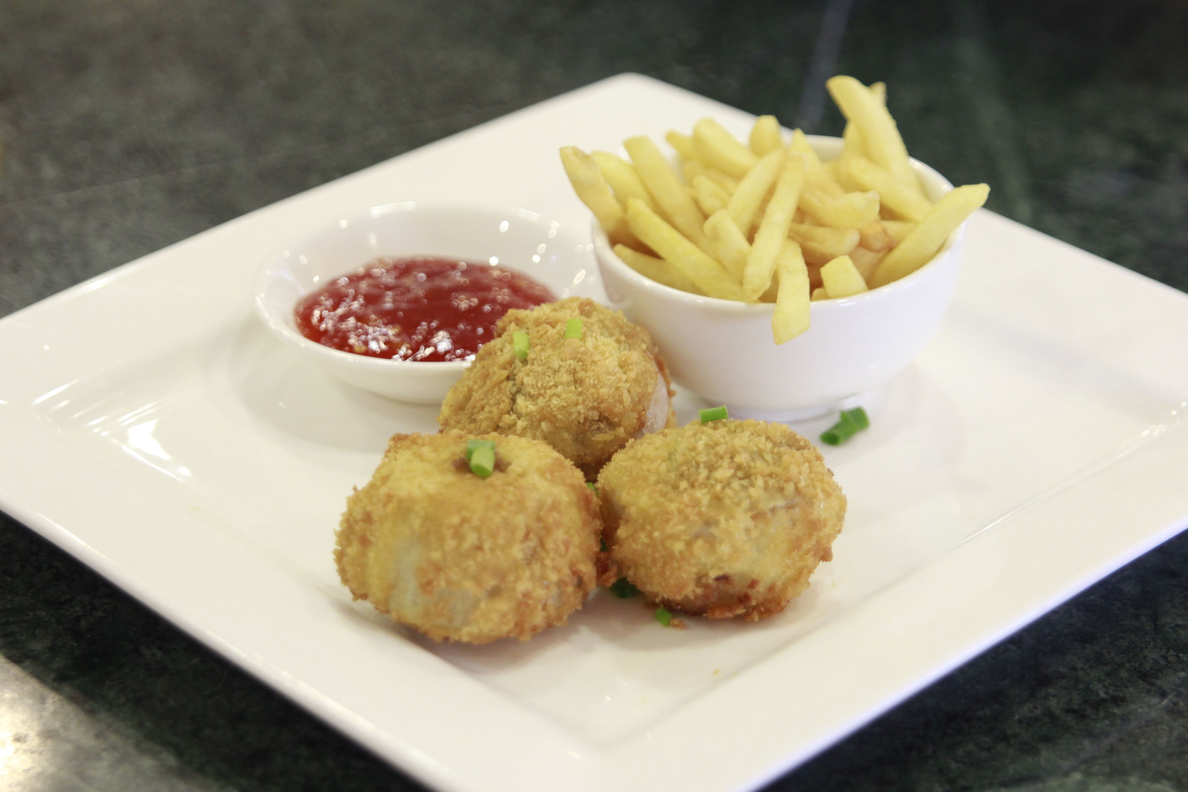 A plate with four breaded items, a bowl of fries, and a small bowl of ketchup.