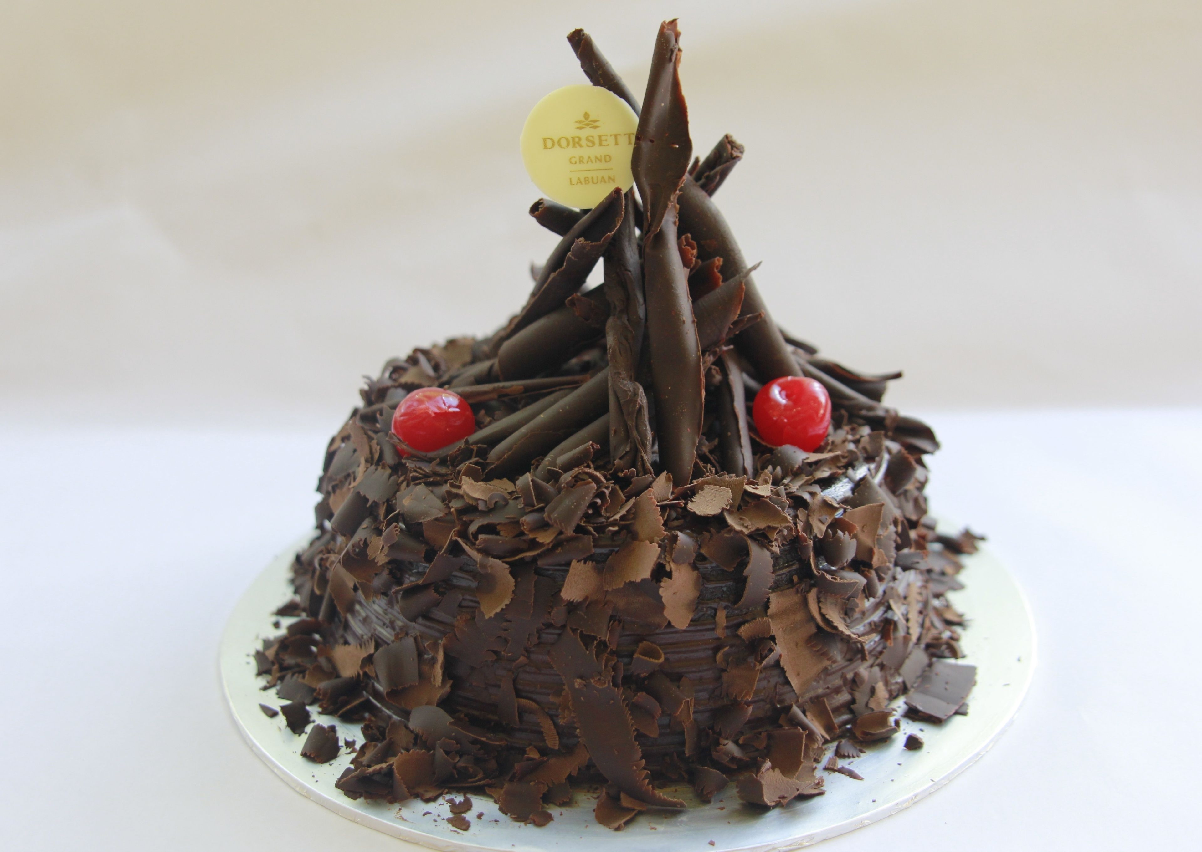 A chocolate cake with a label on top, decorated with chocolate shavings and cherries.