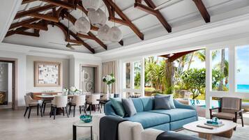 Amplia sala de estar con sofá azul, comedor y grandes ventanales con vista a un paisaje tropical.