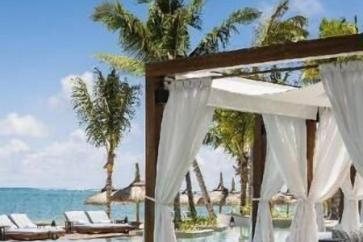 Zona de piscina con una pérgola, sillas de descanso y vista al océano.