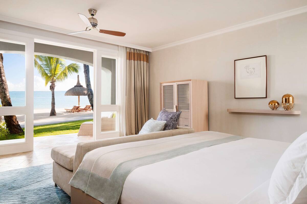 Habitación de hotel con cama, ventilador de techo, vista a la playa y ventana con cortinas.