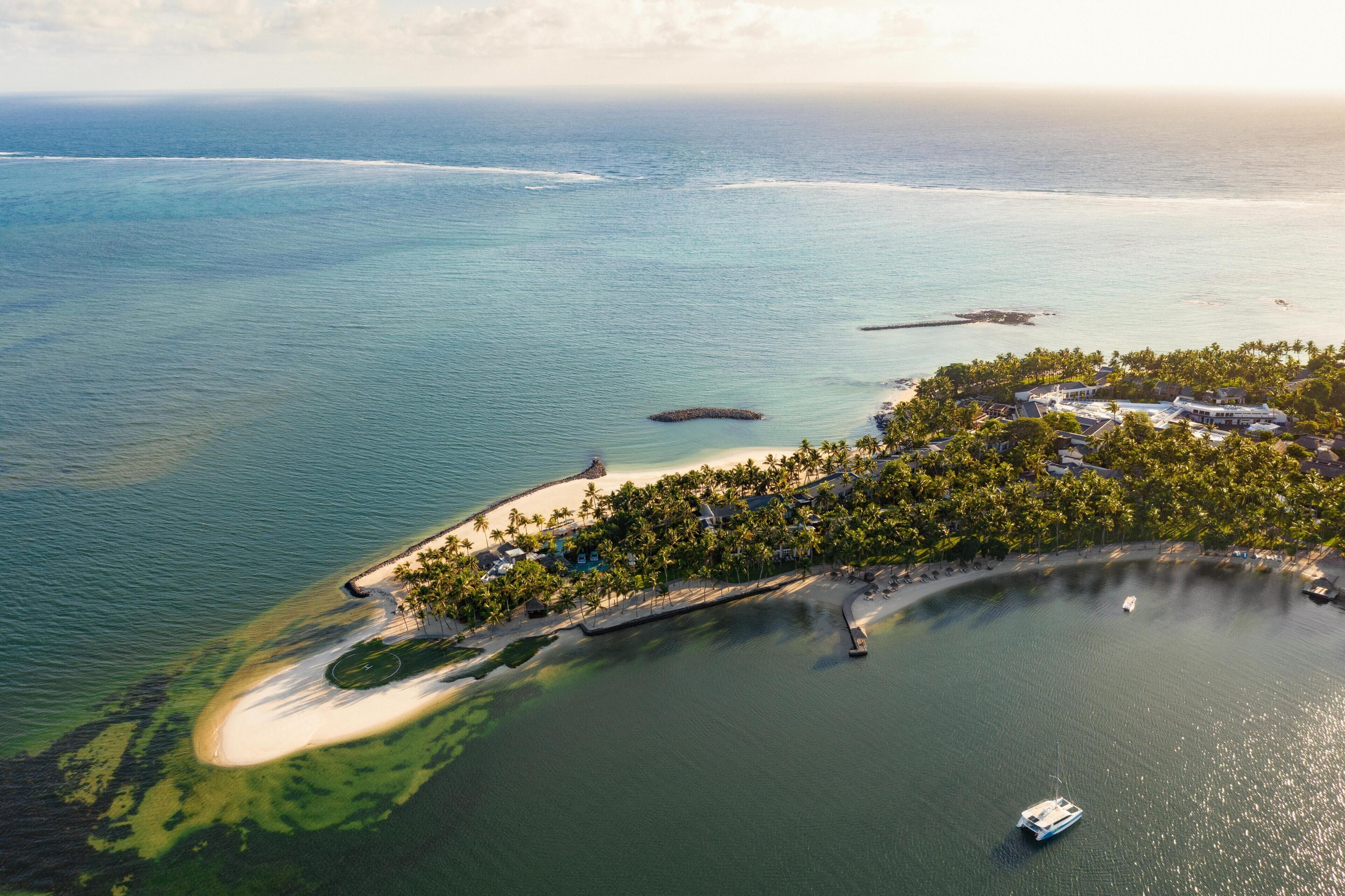 An aerial view of a coastal resort with a sandy beach, a small island with buildings, and a boat in the water.