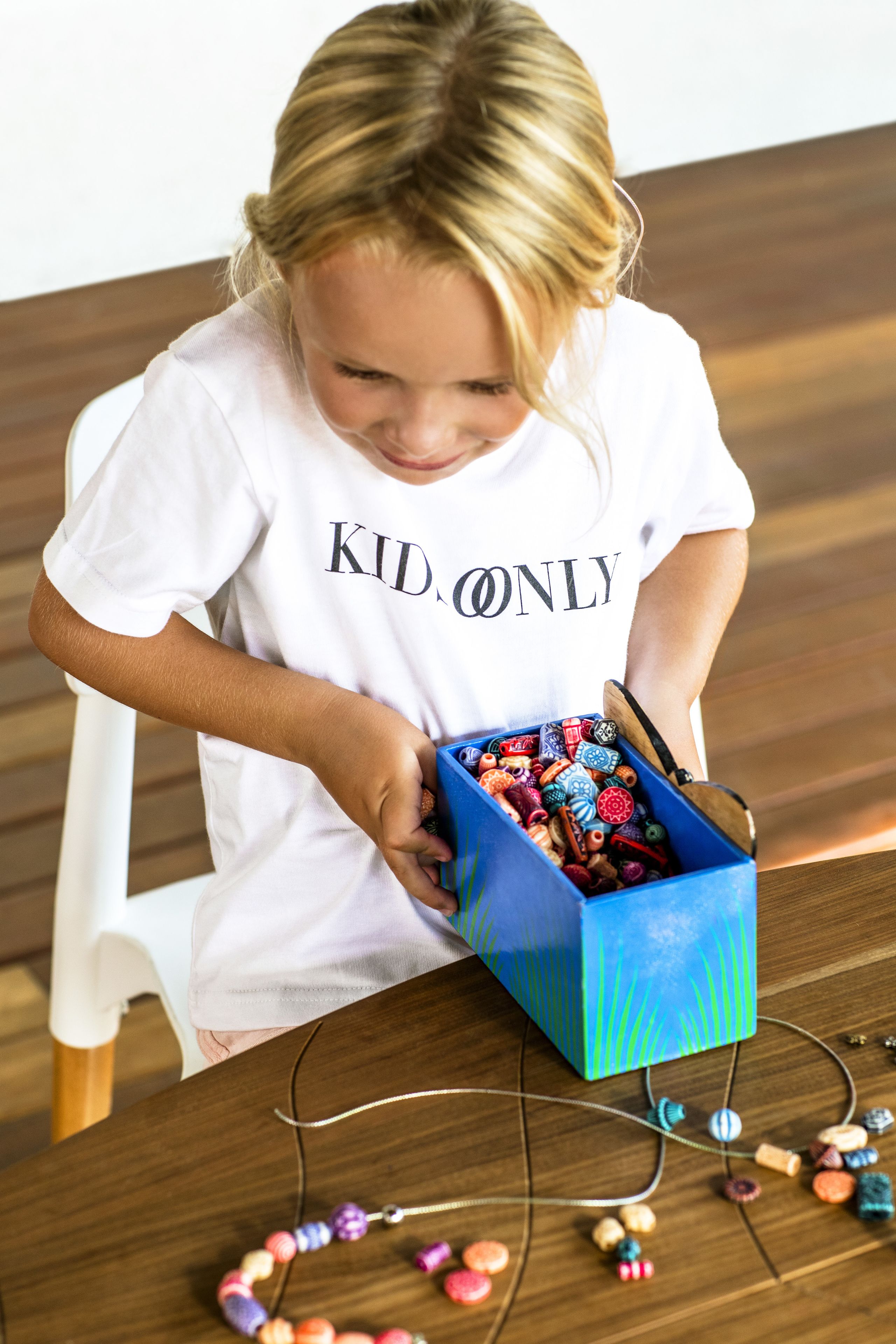 A child sitting at a table with a box of colorful beads.