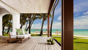 A wooden deck with a white sofa and cushions, palm trees, and a view of the beach. - One&Only Le Saint Géran (Belle Mare)