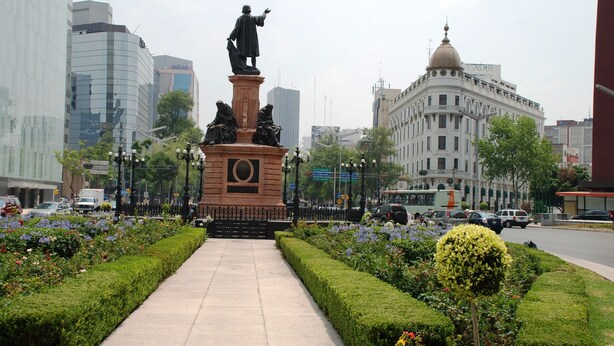 A statue in a city square with a paved walkway, surrounded by neatly trimmed hedges and colorful flowers. - Hotel Imperial Reforma (Mexico City)