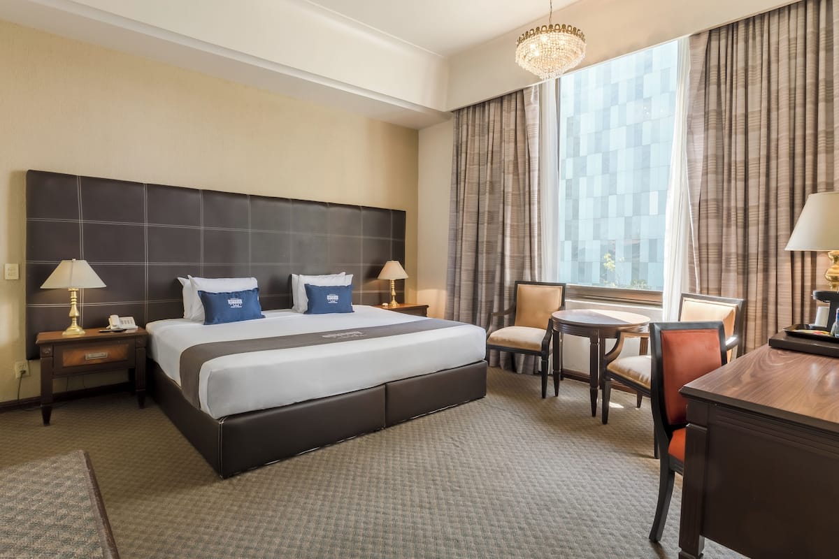 Una habitación de hotel con una cama grande, dos mesitas de noche con lámparas, un escritorio y una silla.
