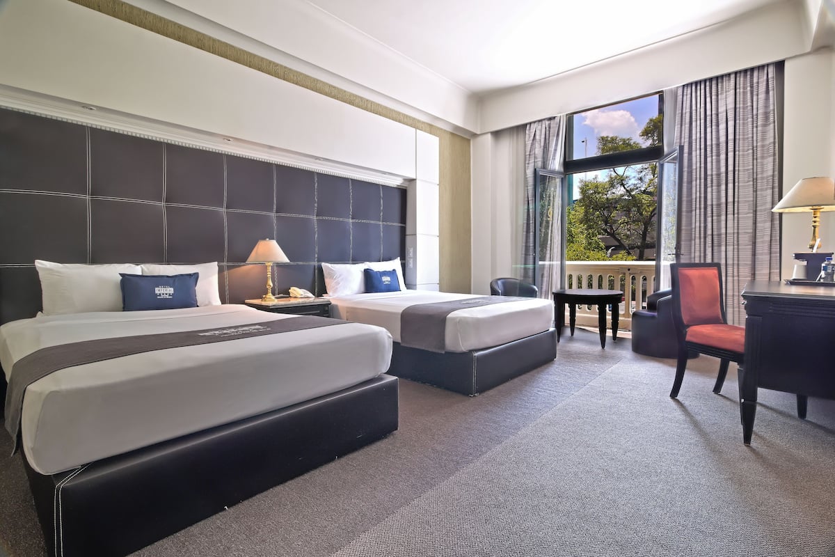 Habitación de hotel con dos camas, un escritorio, una silla y vistas al exterior.