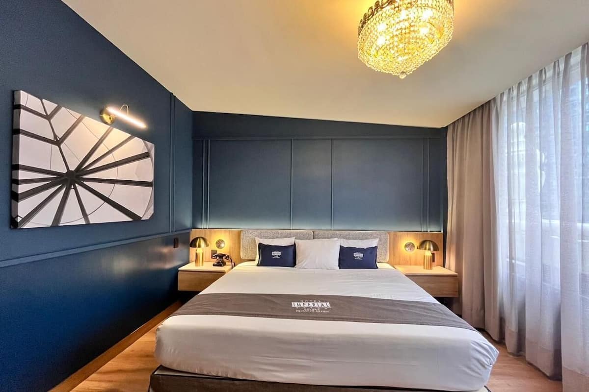 Una habitación de hotel moderna con una cama grande, una araña y vistas de la ciudad.