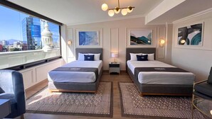 A hotel room with two beds, a desk, a chair, a window with a city view, and a chandelier. - Hotel Imperial Reforma (Mexico City)