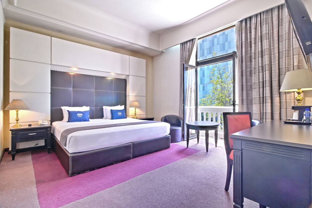 Habitación de hotel con una cama grande, un escritorio, una silla y vistas al exterior.