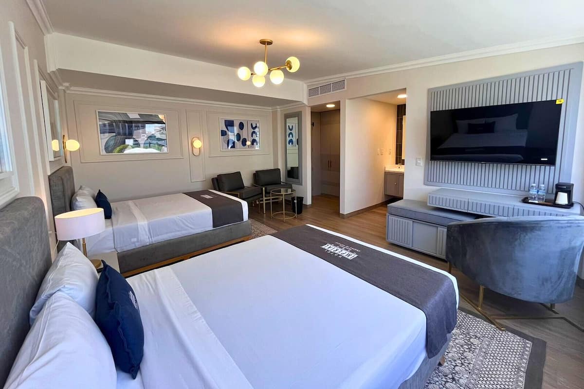 Habitación de hotel con dos camas, televisión, escritorio y zona de estar.
