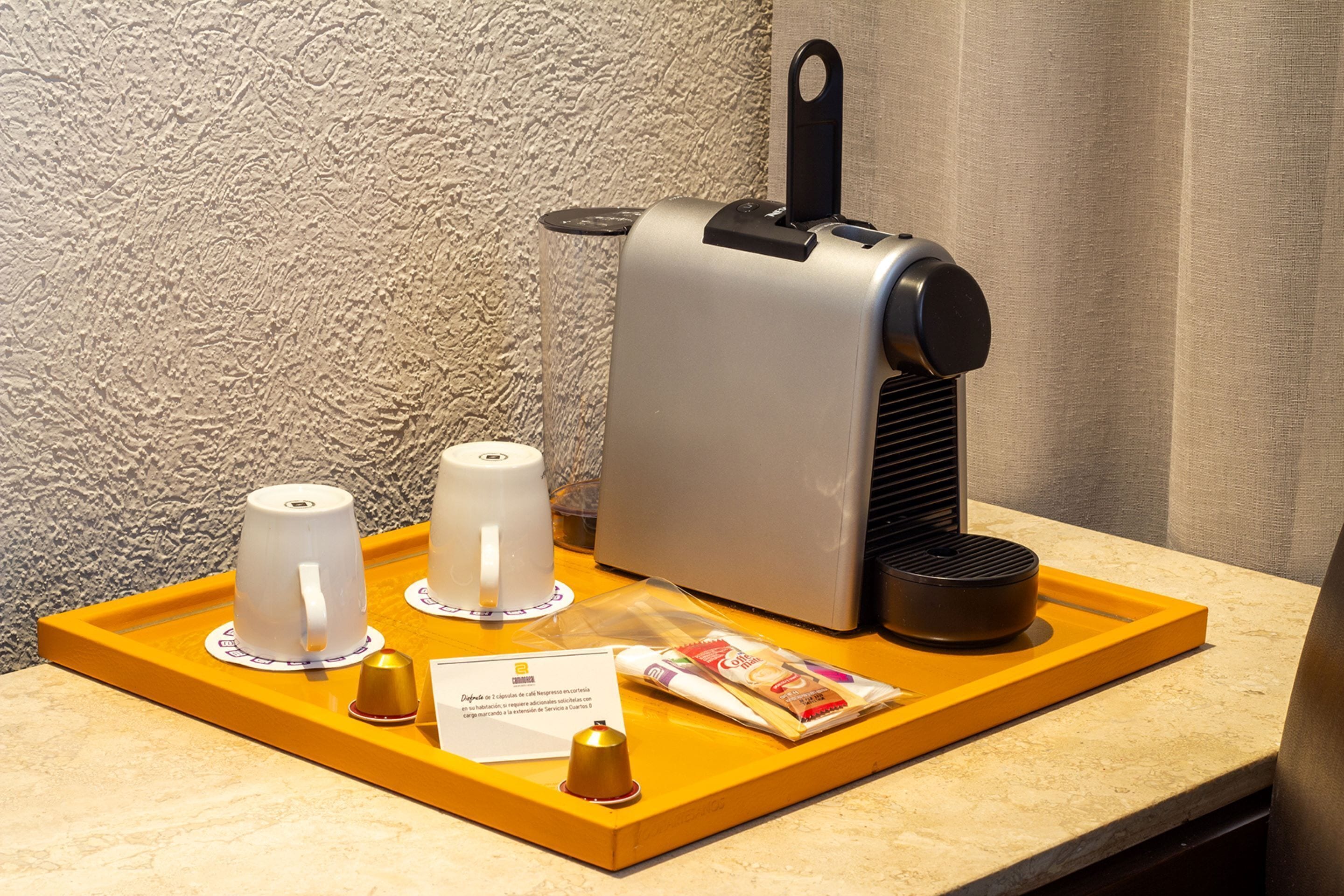 Een koffiehoek met een koffieapparaat, twee kopjes, een dienblad, een bel en een menukaart.