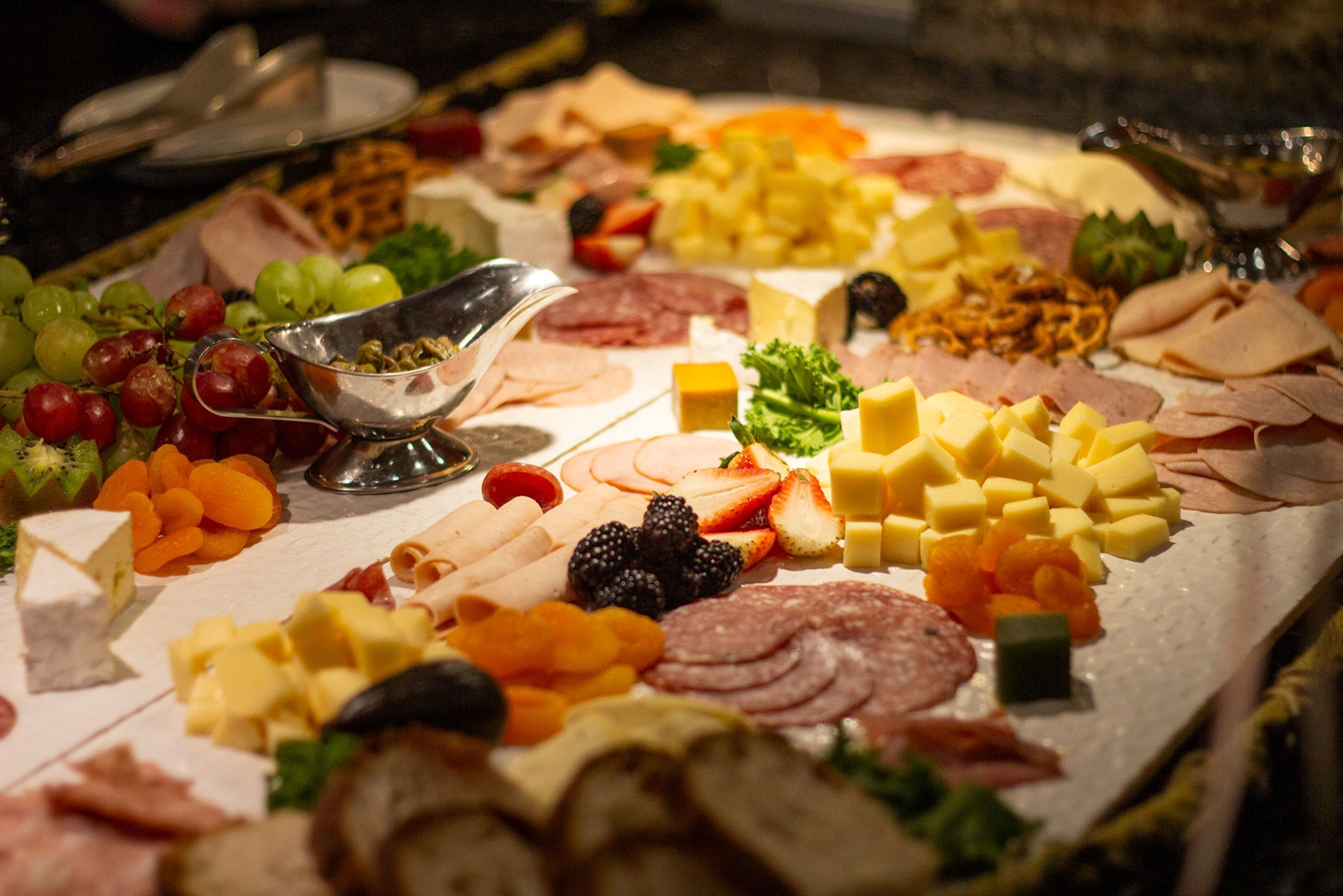 Una tabla de fiambres con varios quesos, carnes, frutas y verduras.