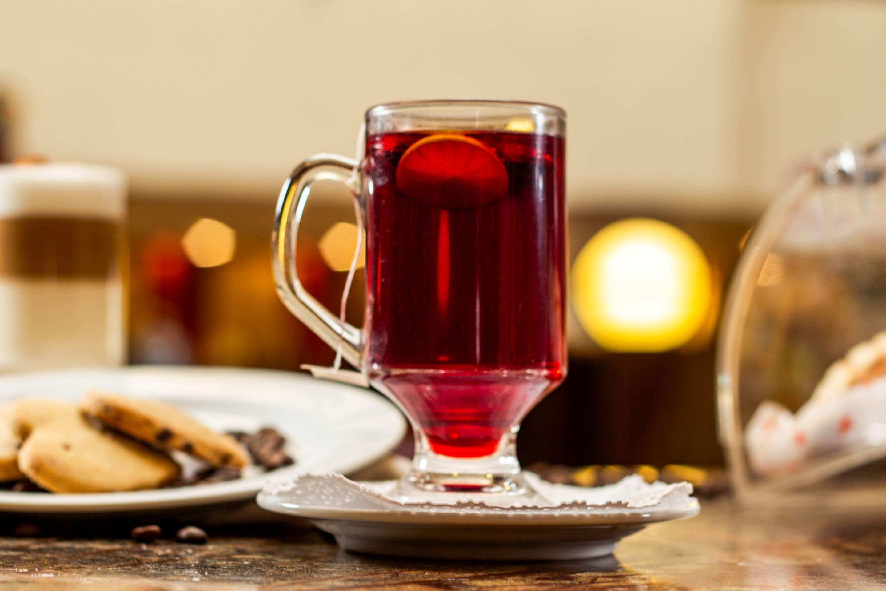 Una taza de vidrio transparente con asa, llena de una bebida roja, sobre un platito.