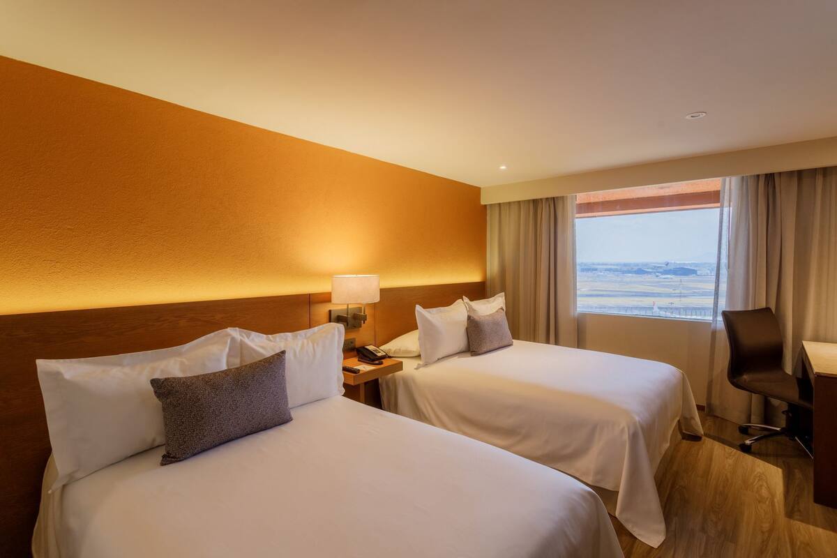 A hotel room with two beds, a desk, a chair, and a view of the beach.