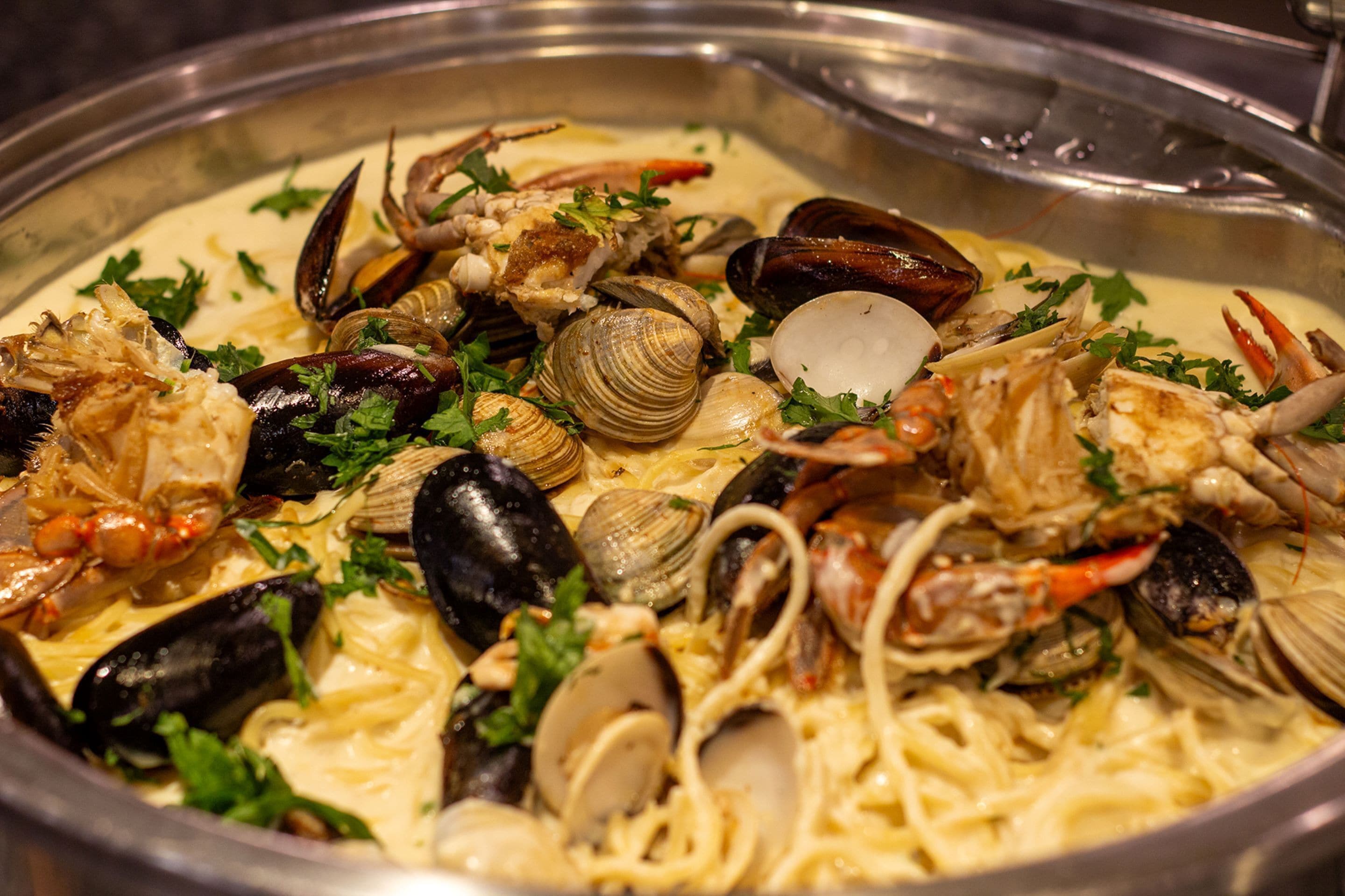 Prato de massa de frutos do mar com amêijoas, mexilhões e caranguejo, decorado com salsa.