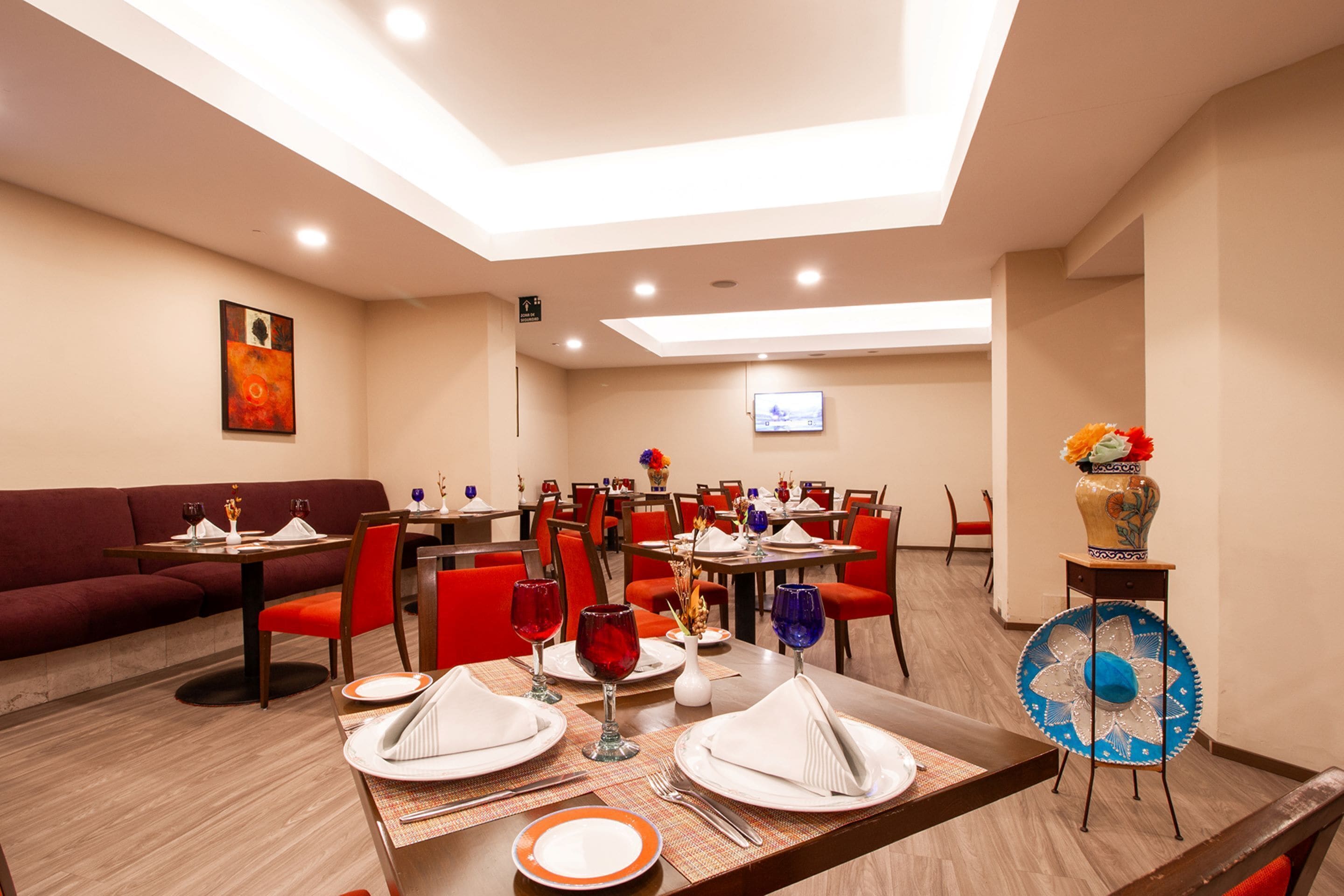 A dining area with tables set for four, red chairs, and a blue fan.