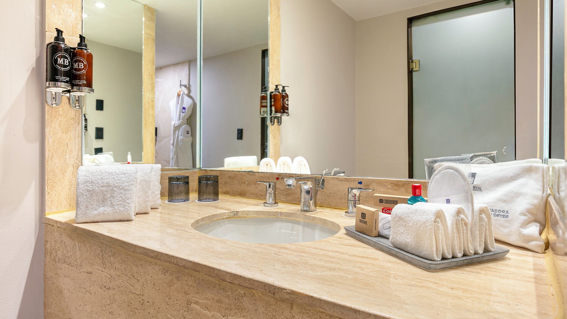 A bathroom with a marble sink, two faucets, a large mirror, and toiletries on the counter.