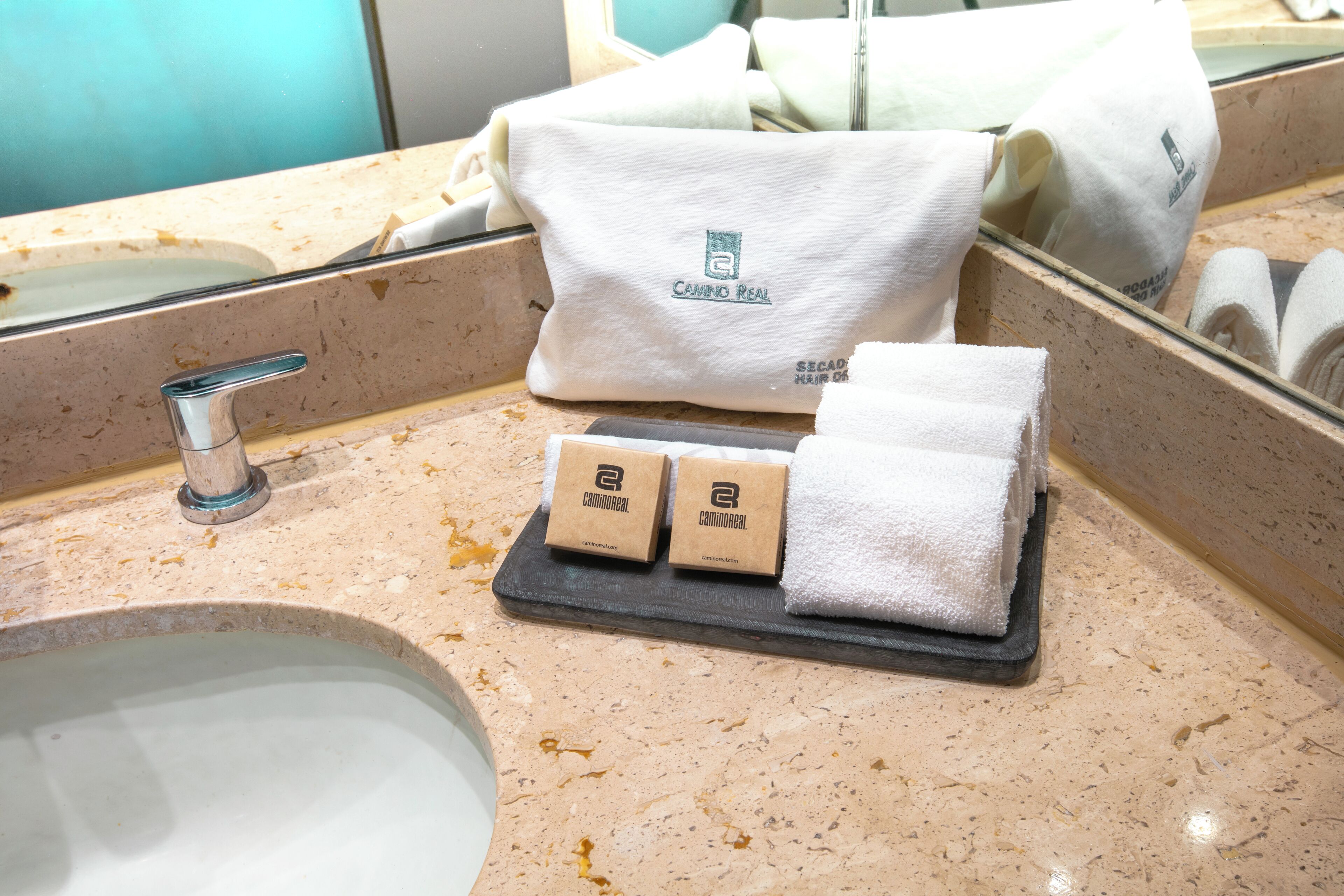 A bathroom with a sink, a towel, and two small boxes on a tray.