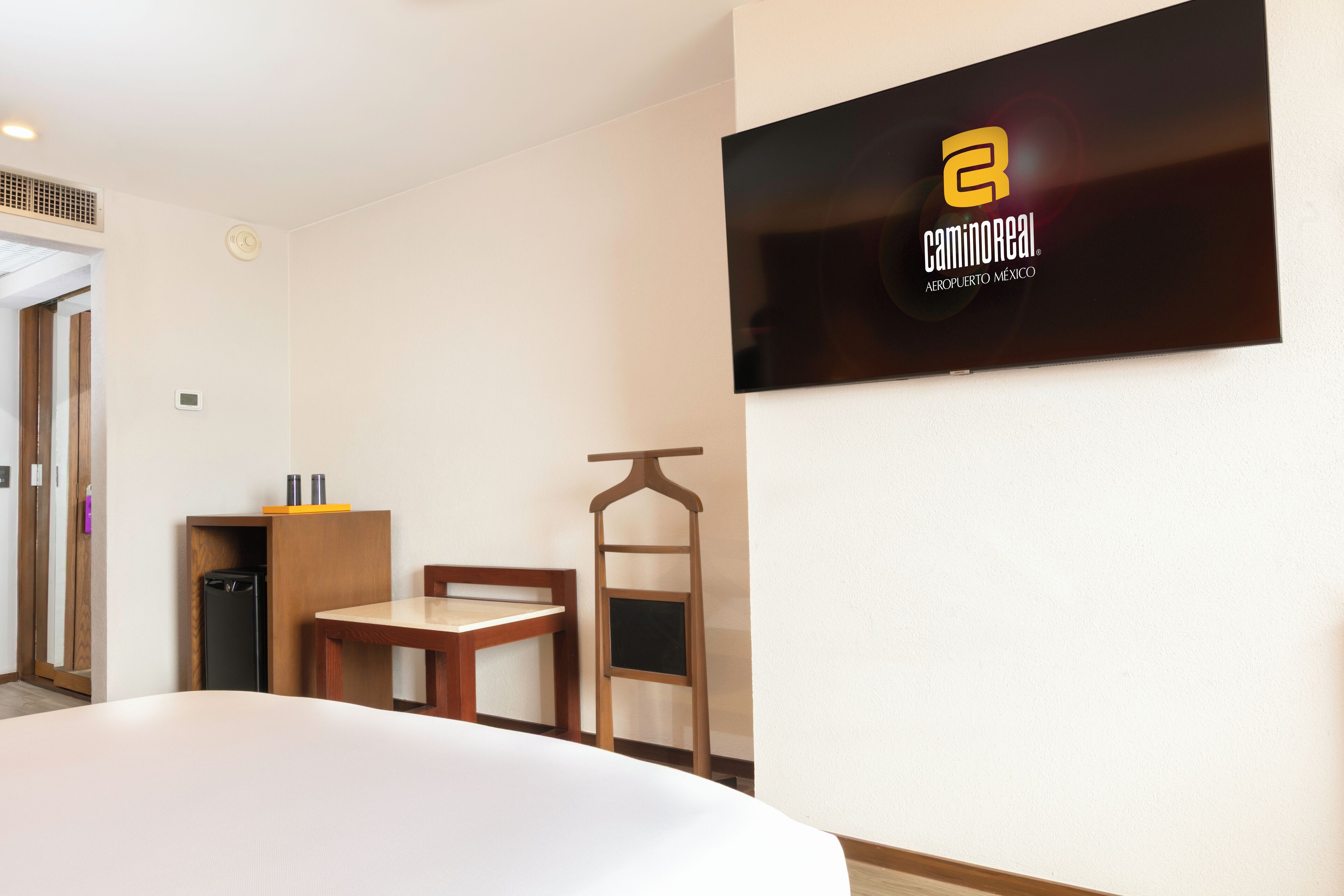 Une chambre d’hôtel avec un lit, une petite table, une chaise, un téléviseur fixé au mur et une armoire en bois.