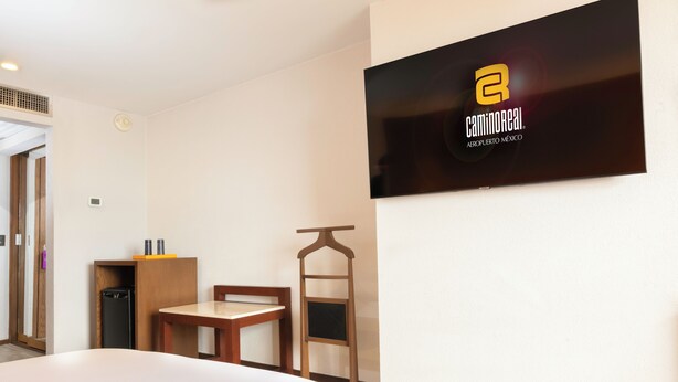 A hotel room with a bed, a desk, a chair, a small table, a television mounted on the wall, and a wardrobe.