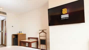 A hotel room with a bed, a small table, a chair, a TV mounted on the wall, and a wooden cabinet.