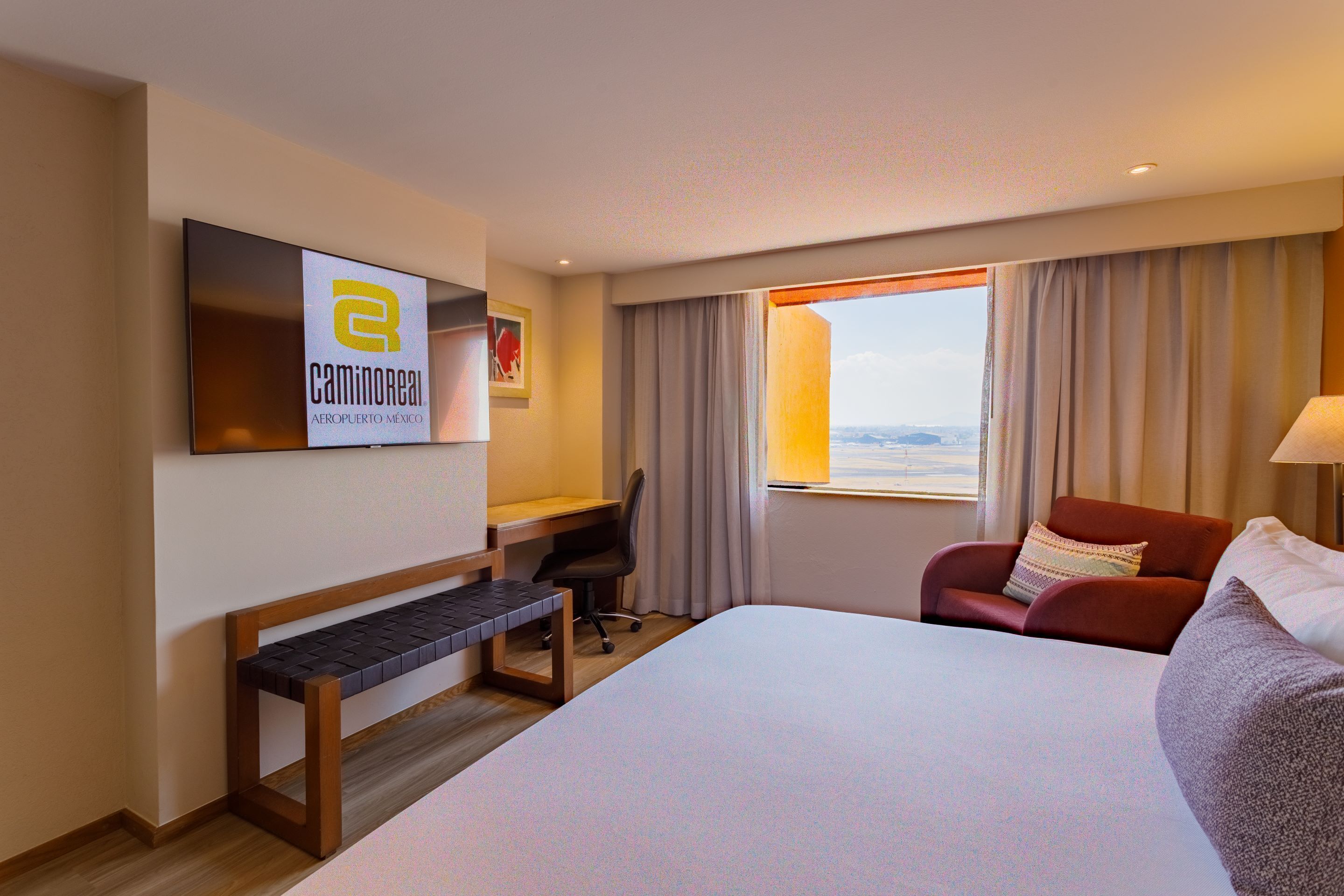 Habitación de hotel con cama, escritorio, silla y un amplio ventanal con vistas.