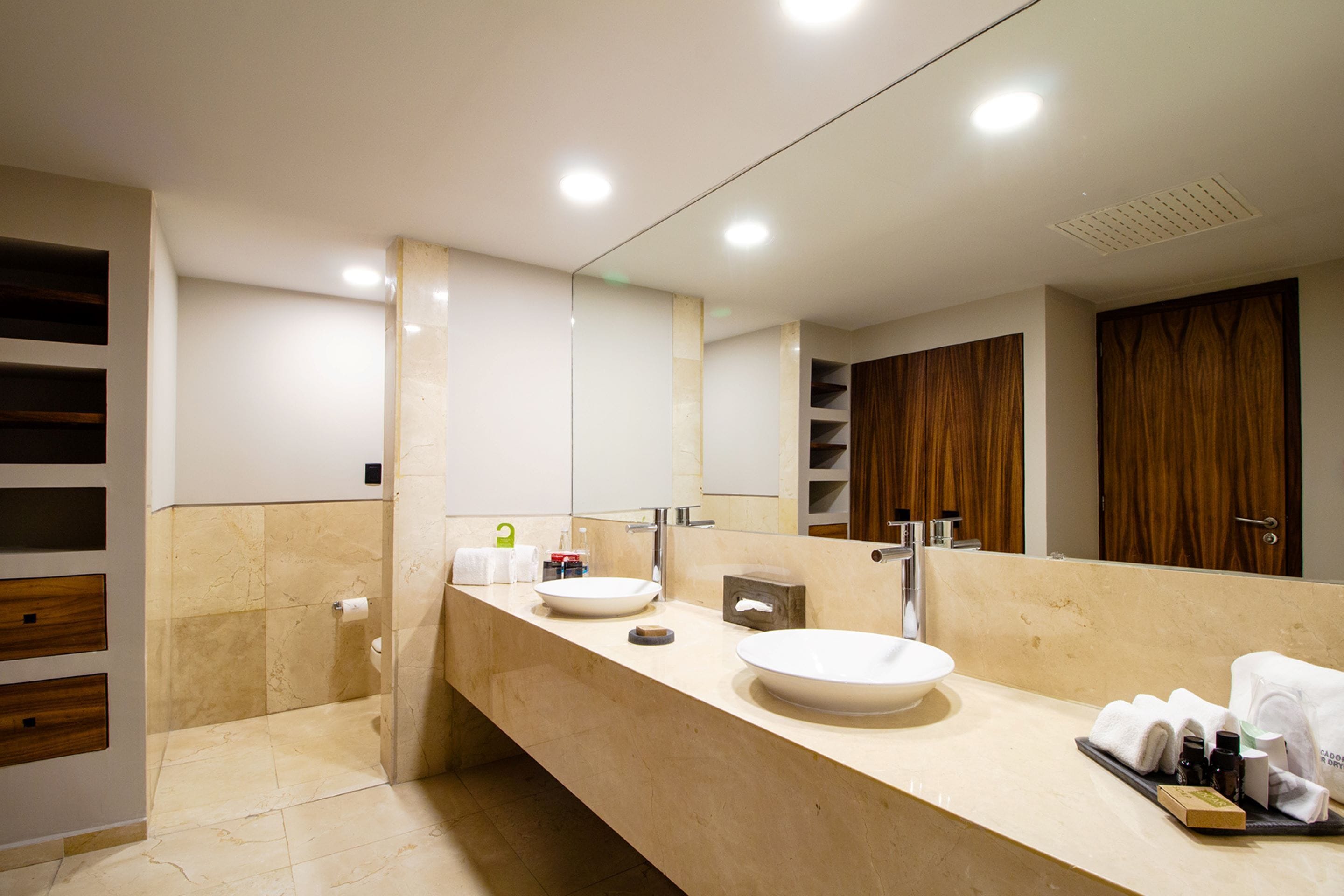 A modern bathroom with a large mirror, two sinks, and a vanity with storage.