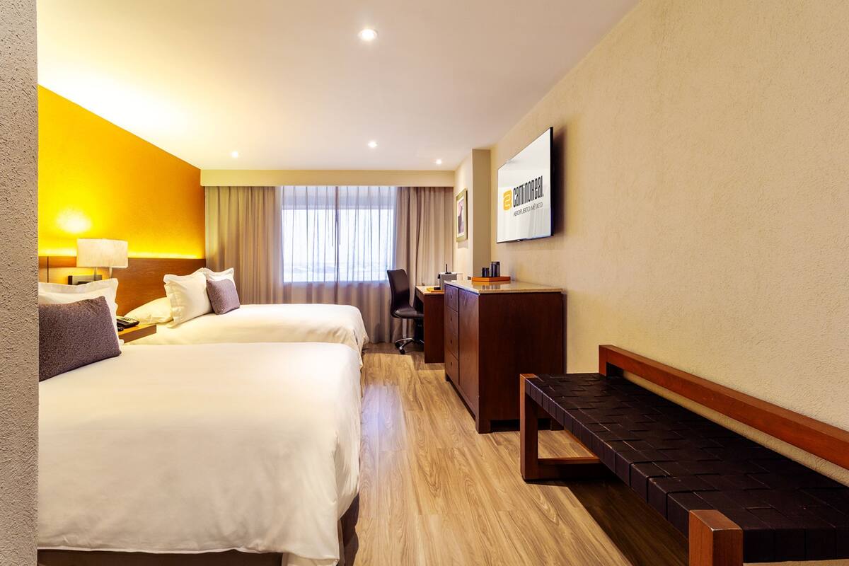A hotel room with two beds, a desk, a chair, and a bench.